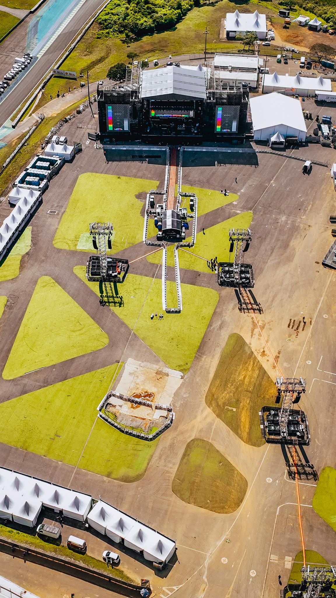 Reviews Aerial view of a large outdoor concert stage being set up in a sunny location.